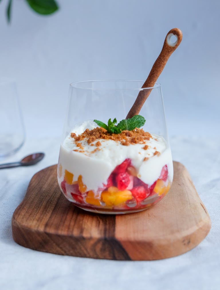 A close-up of a creamy yogurt parfait with fresh fruit layers, granola, and mint.