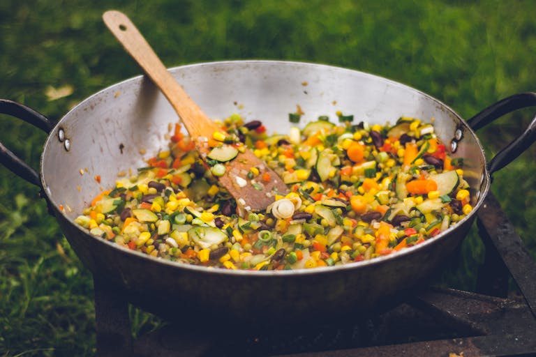 A vibrant outdoor cooking scene with fresh vegetables in a pan.