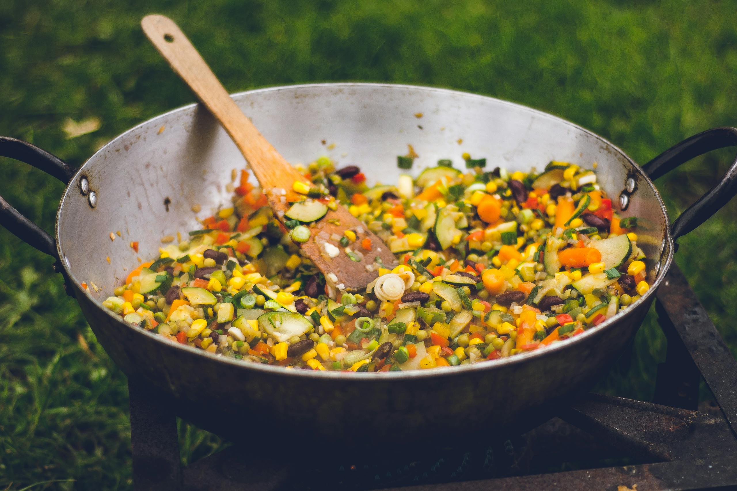 A vibrant outdoor cooking scene with fresh vegetables in a pan.