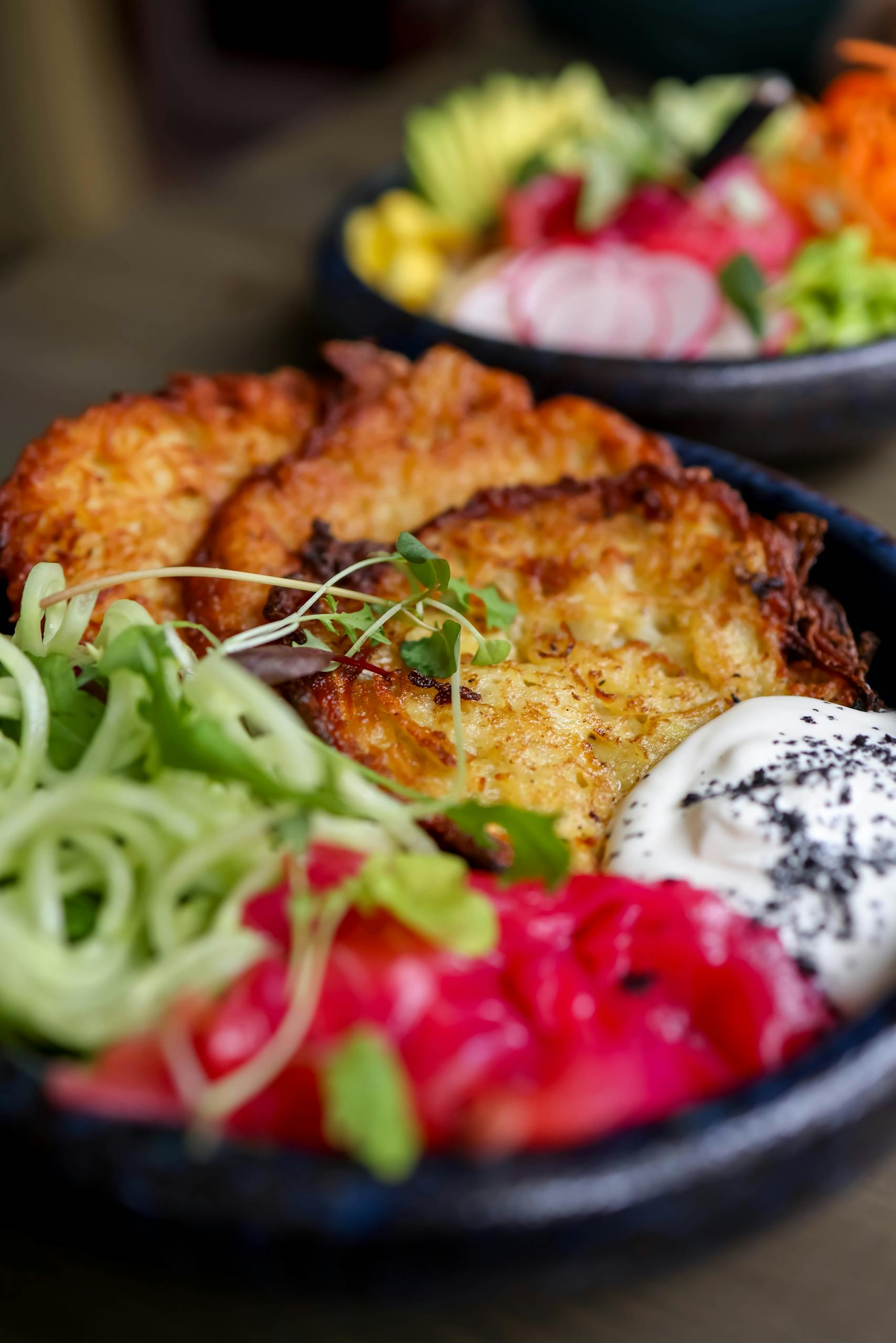 Close-up of a colorful veggie fritter bowl with fresh toppings and sour cream.