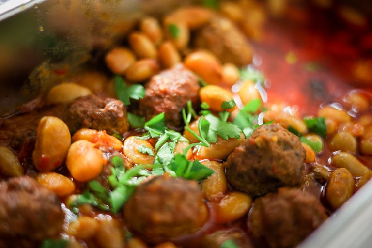 Close-up of a mouth-watering bean and meatball stew garnished with fresh herbs.