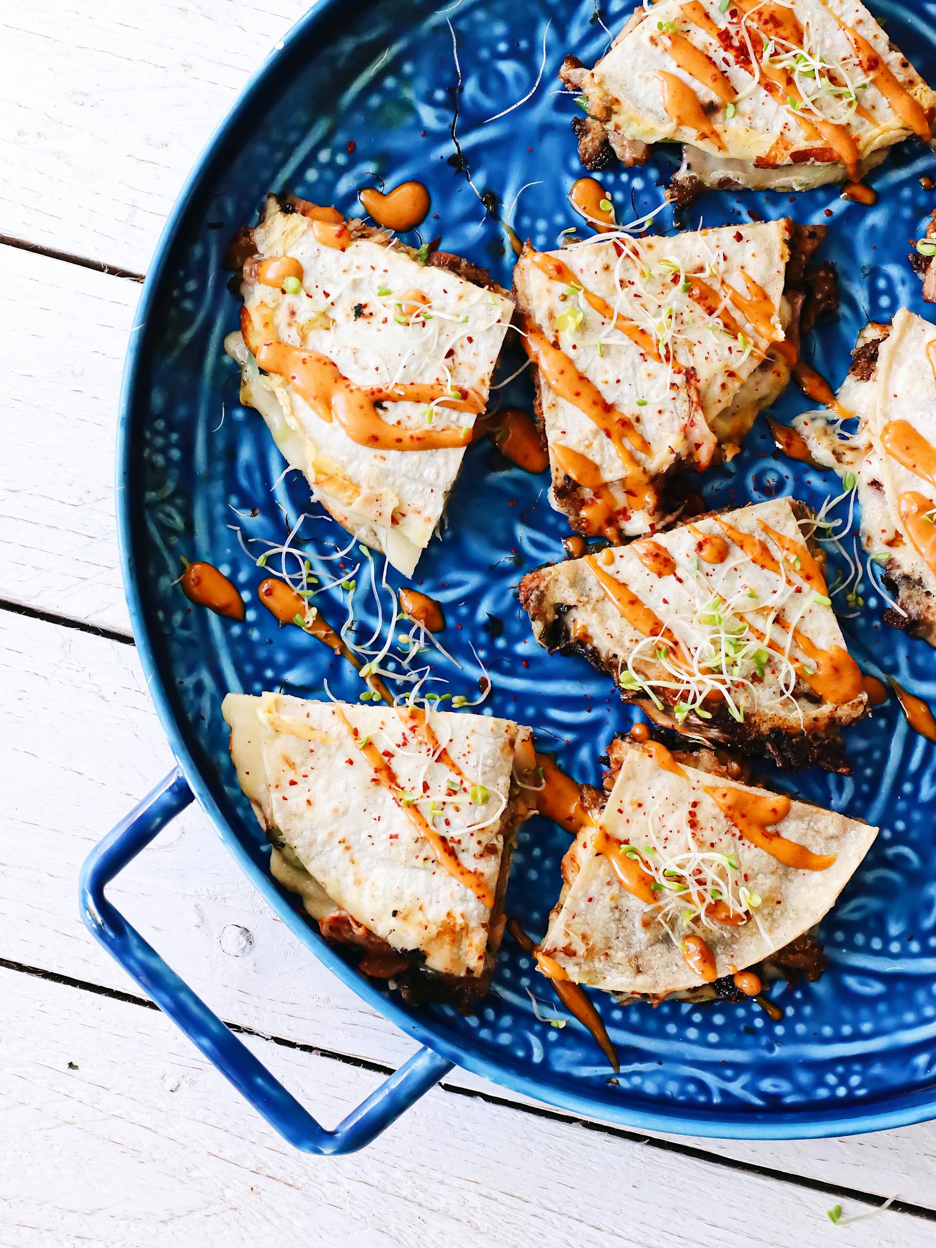 Overhead delicious triangle tortillas with vegetables topped with fresh sauce and served on blue ornamental plate